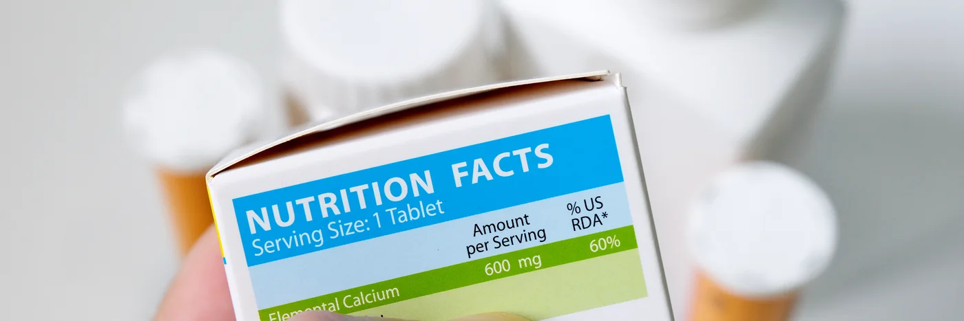 A hand holding a supplement carton turned to show the Nutrition Facts panel on the back.